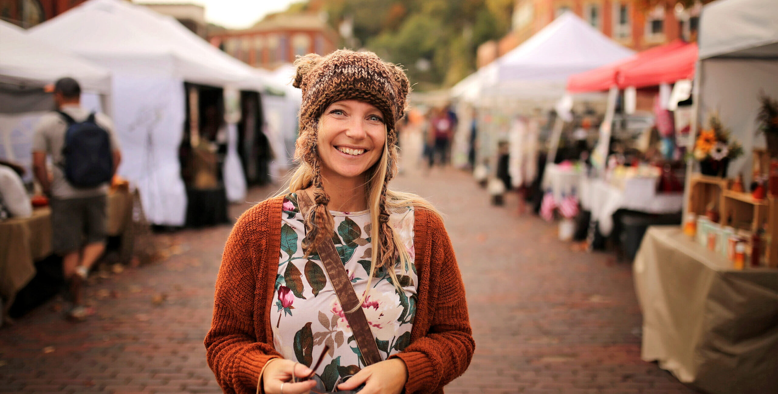 A woman in a hat and sweater standing on the street.