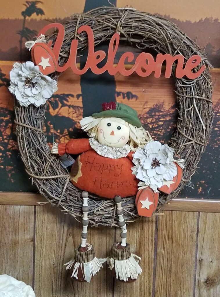 A wreath with a scarecrow and bells hanging from it.