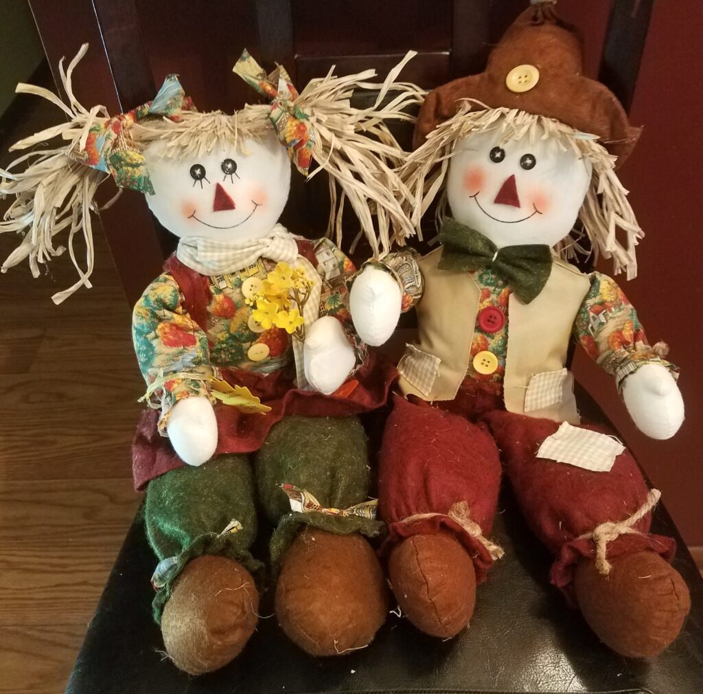 Two scarecrows sitting on a chair next to each other.