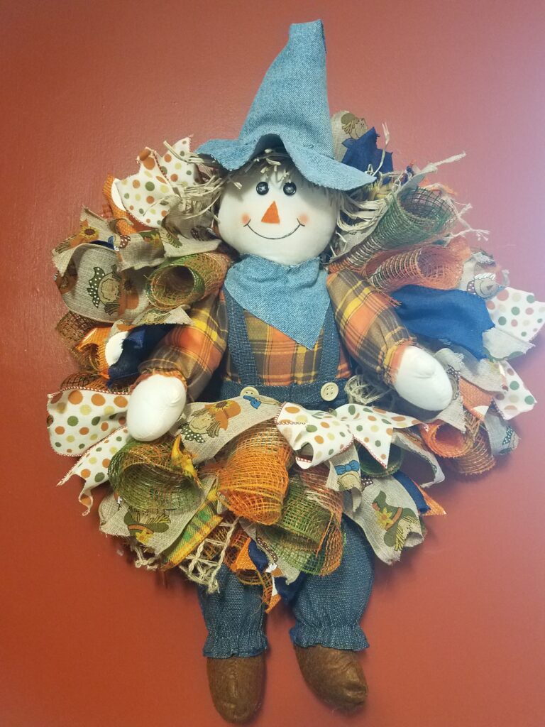 A scarecrow wreath is made of fabric and has a blue hat.