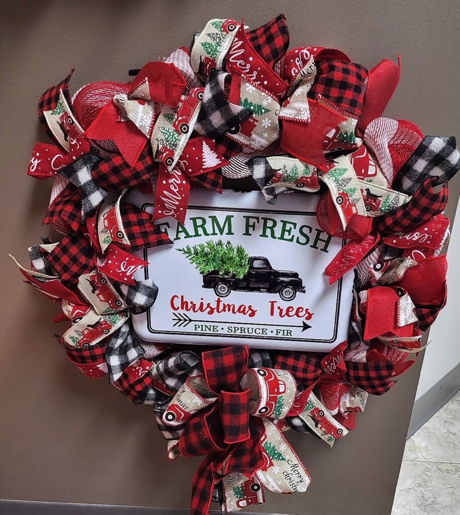 A wreath with ribbon and a sign that says farm fresh christmas trees.