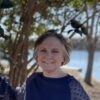 Woman smiling outdoors, near trees.