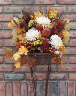 A flower arrangement in a basket on top of a brick wall.