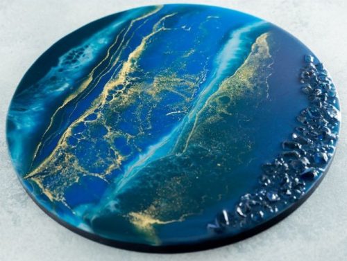 A blue and gold round coaster with a picture of the ocean.